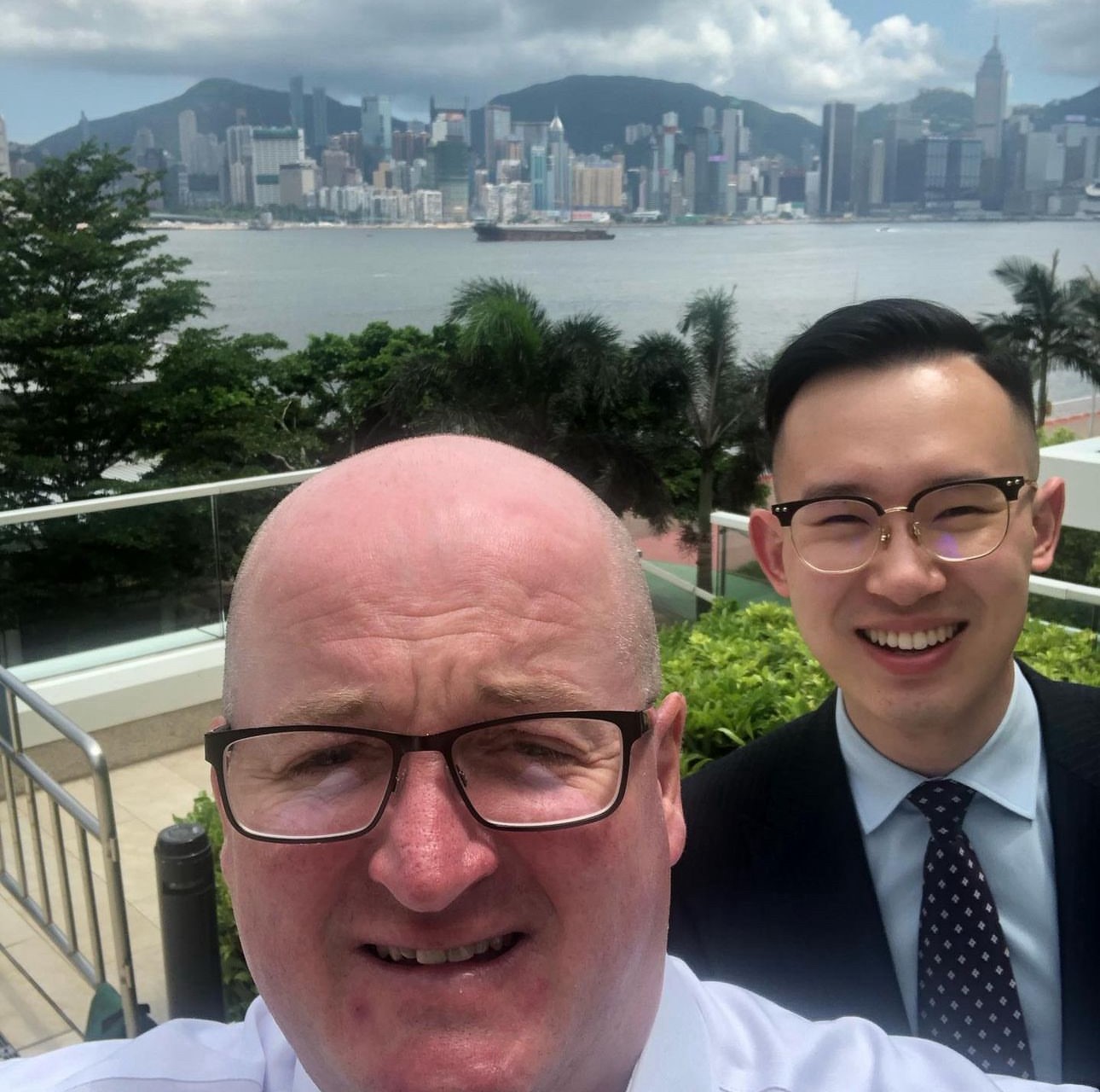 Selfie of Marcus Ward and Ziqiao Chen on a balcony with Hong Kong seen in the distance behind them.