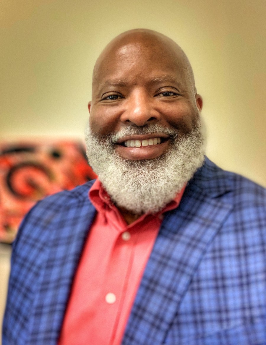 Headshot of Kenneth Cooper, a Black man wearing a red shirt and a blue checked blazer.