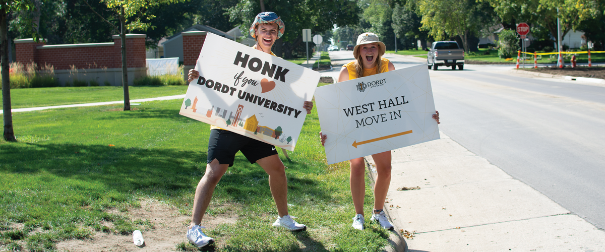 Two Dordt students, dressed in summer clothes, hold signs for move-in day at the university.