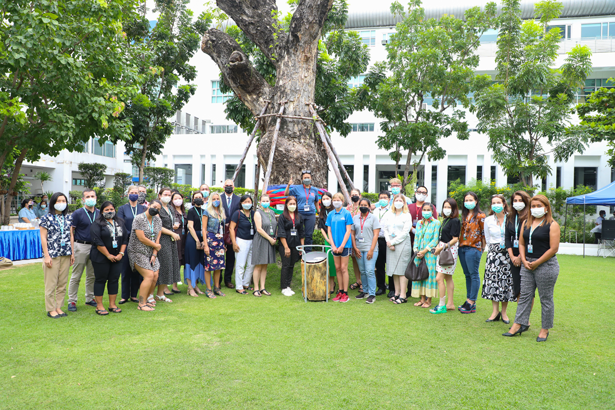 Students and faculty at NIST International School stand around an iconic tree on campus.