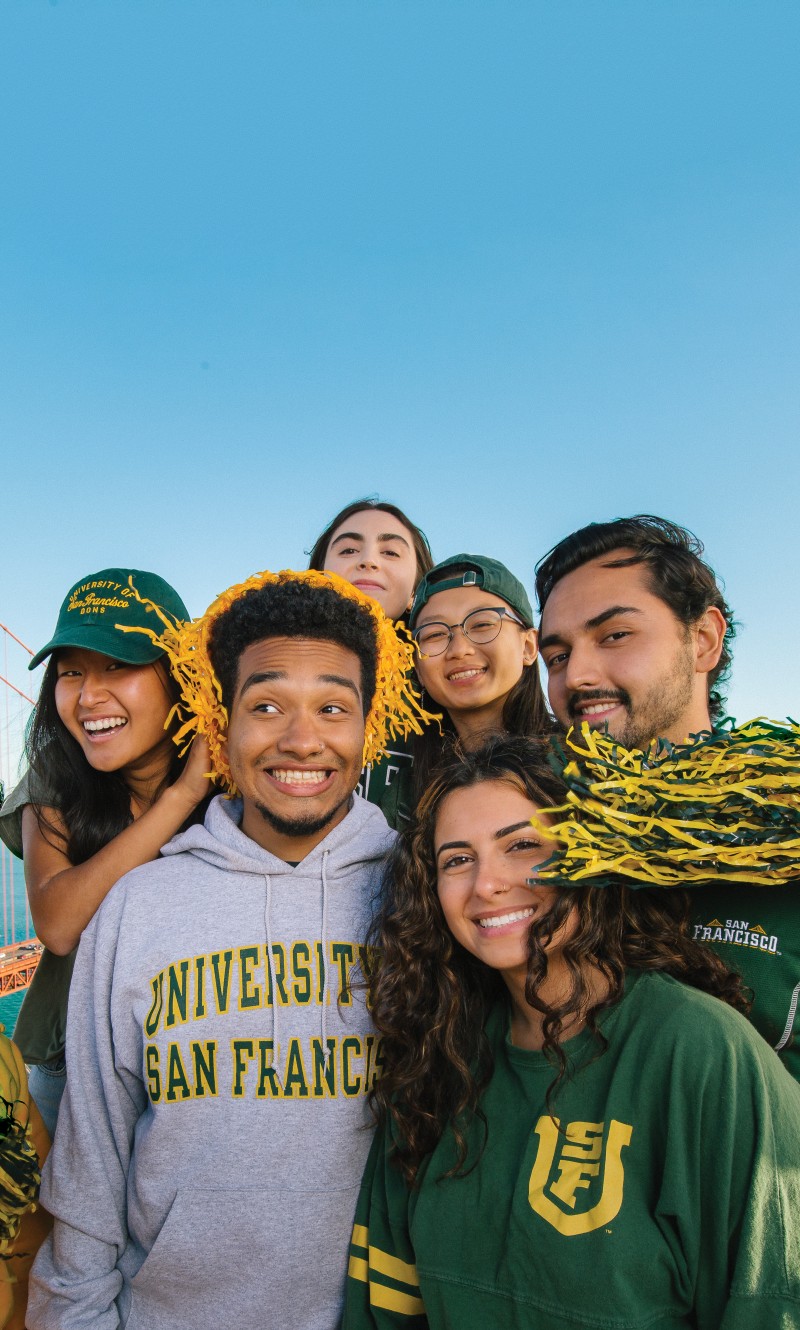 A group of University of San Francisco students in USF merch against a blue sky