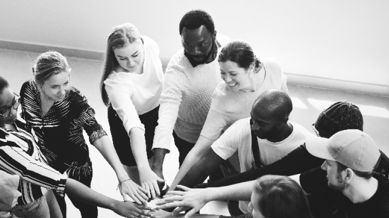 Mixed race group putting their hands together in the center of a circle