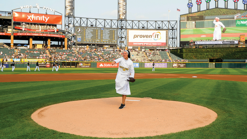 Nun in habit, with school t-shirt over it, and mitt throws from the mound
